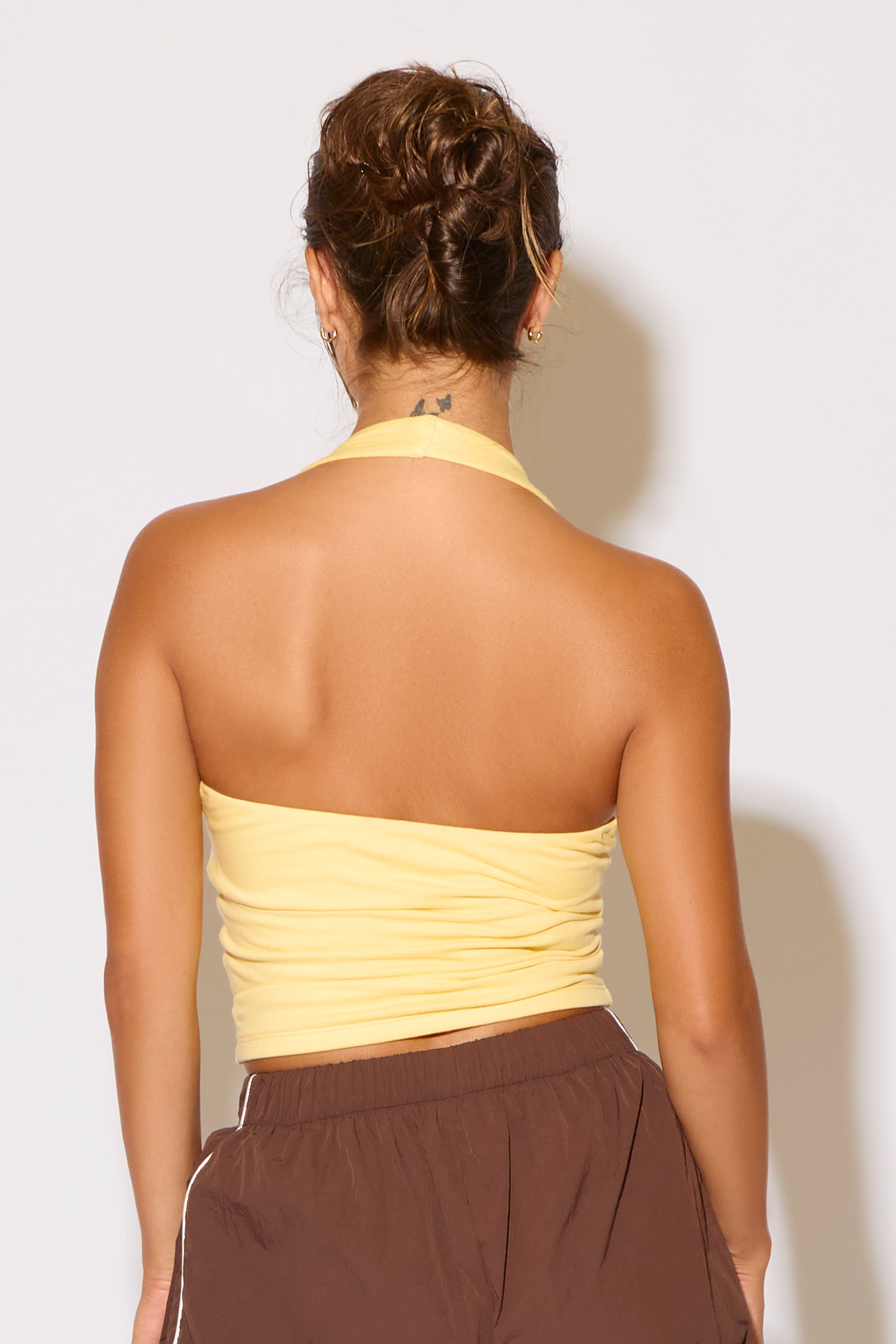 Person wearing a yellow strapless top and brown pants against a white background
