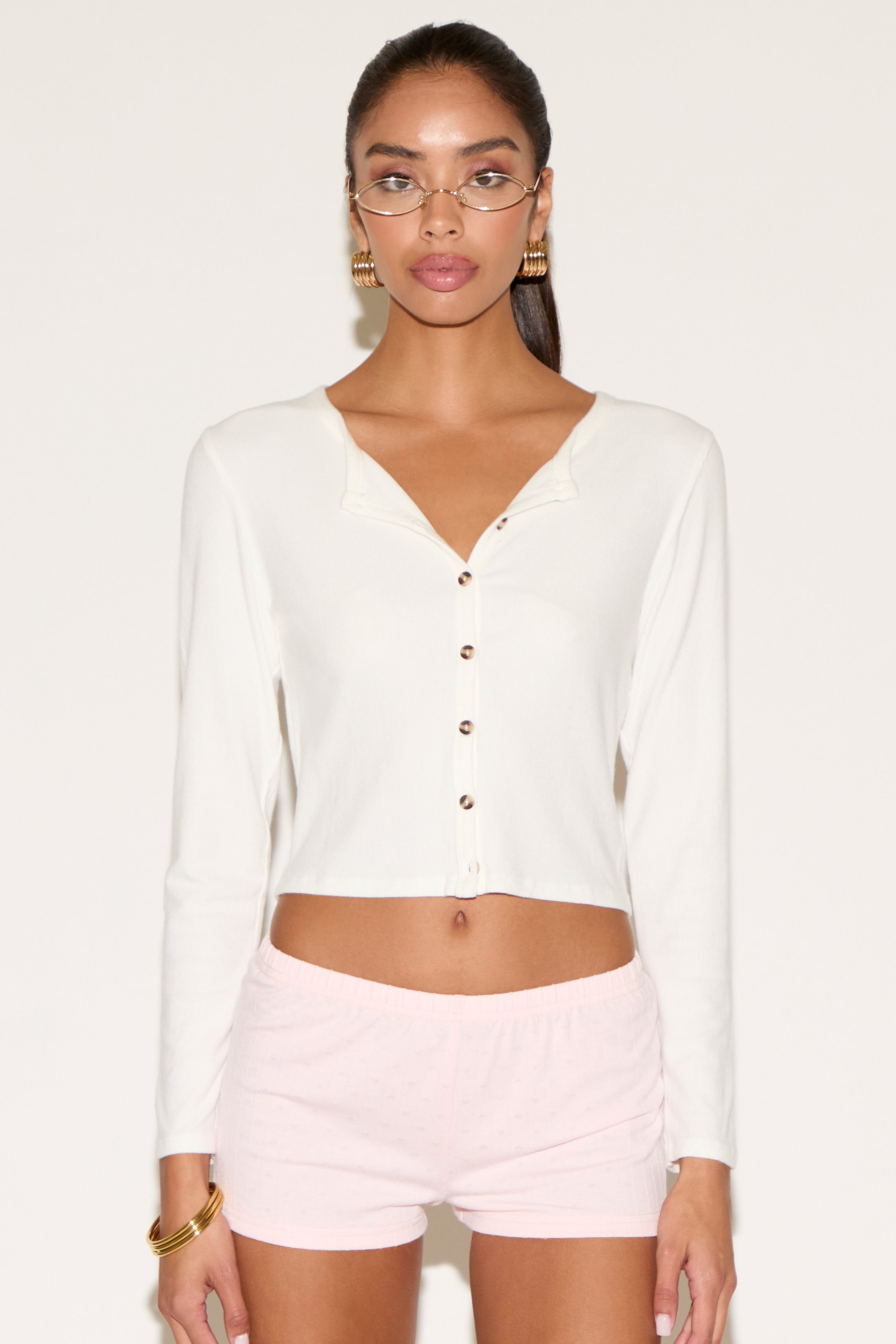Woman wearing a white long-sleeve top and pink shorts on a white background