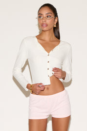Woman wearing a white cardigan and pink shorts on a plain background