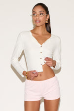 Woman wearing a white cardigan and pink shorts on a plain background