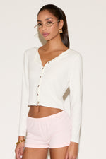 Woman wearing a white long-sleeve top and light pink shorts on a plain background