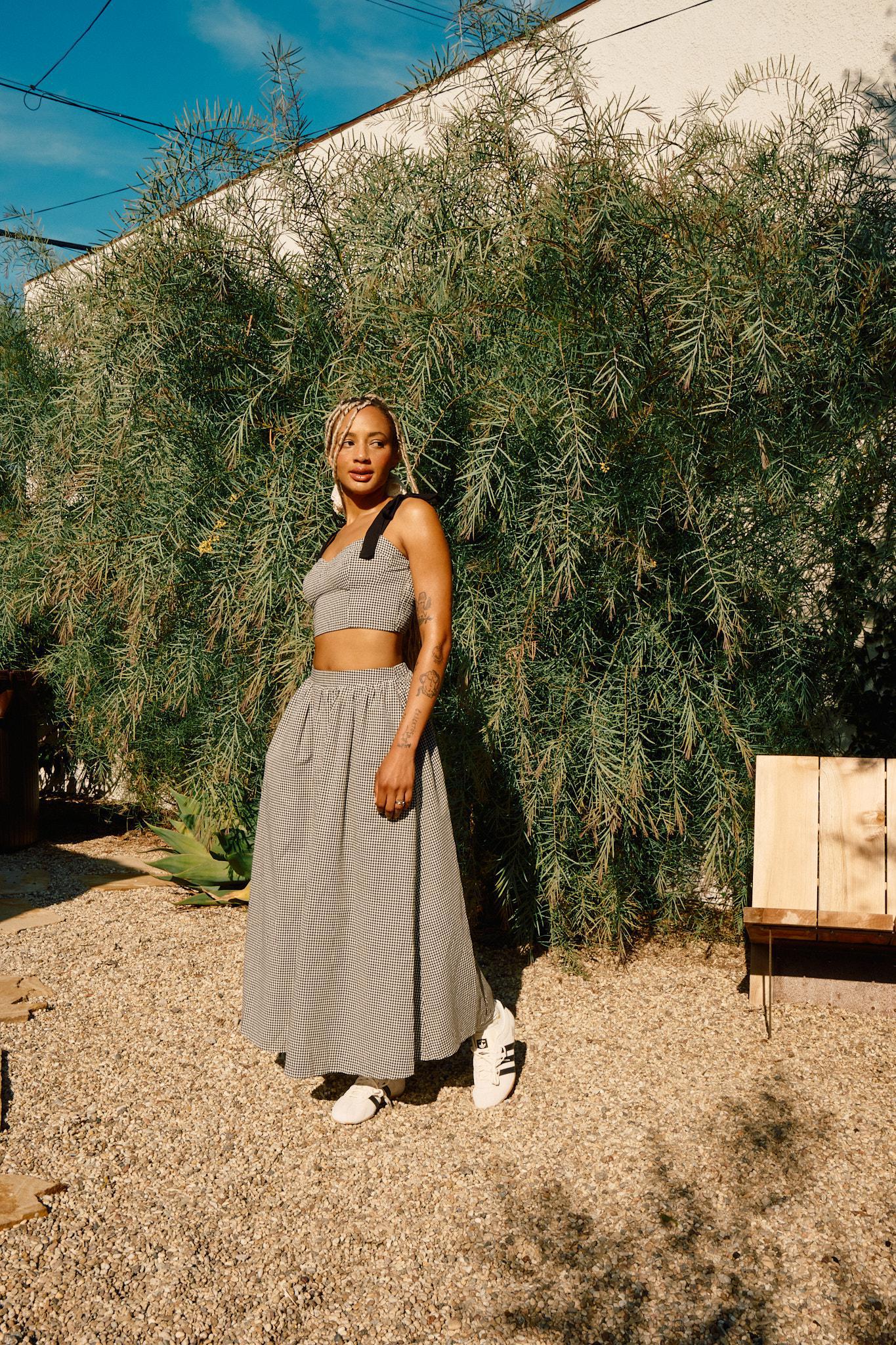 A person wearing a high rise black and white checkered maxi skirt with a crop top and white sneakers standing outdoors.