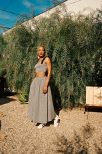 A person wearing a high rise black and white checkered maxi skirt with a crop top and white sneakers standing outdoors.