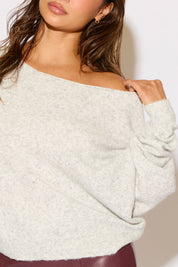 Close-up of a person wearing an off-shoulder sweater with a neutral background