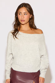 Woman wearing a light gray off-shoulder sweater with maroon pants on a white background