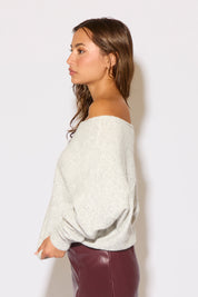 Woman wearing a light gray off-shoulder top against a white background