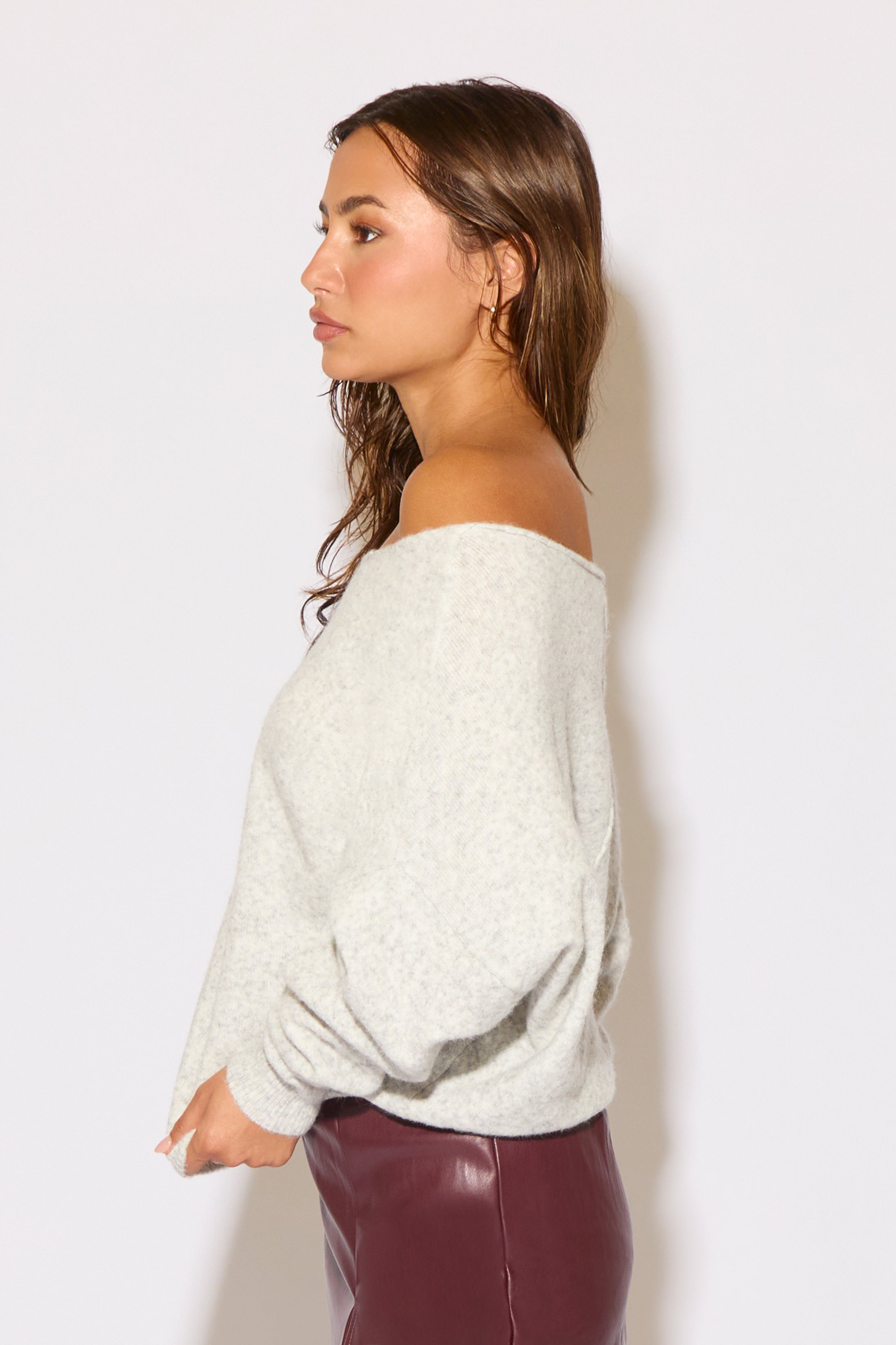 Woman wearing a light gray off-shoulder top against a white background