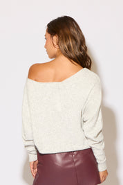 Woman wearing a white off-shoulder sweater and maroon leather skirt against a light background