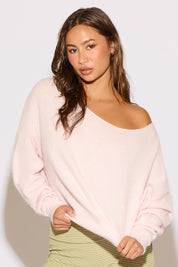 Woman wearing a light pink off-shoulder sweater against a plain background