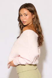 Woman wearing a light pink off-shoulder top and green pants against a white background