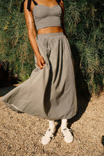 A person wearing a high rise black and white checkered maxi skirt with a crop top and white sneakers standing outdoors.