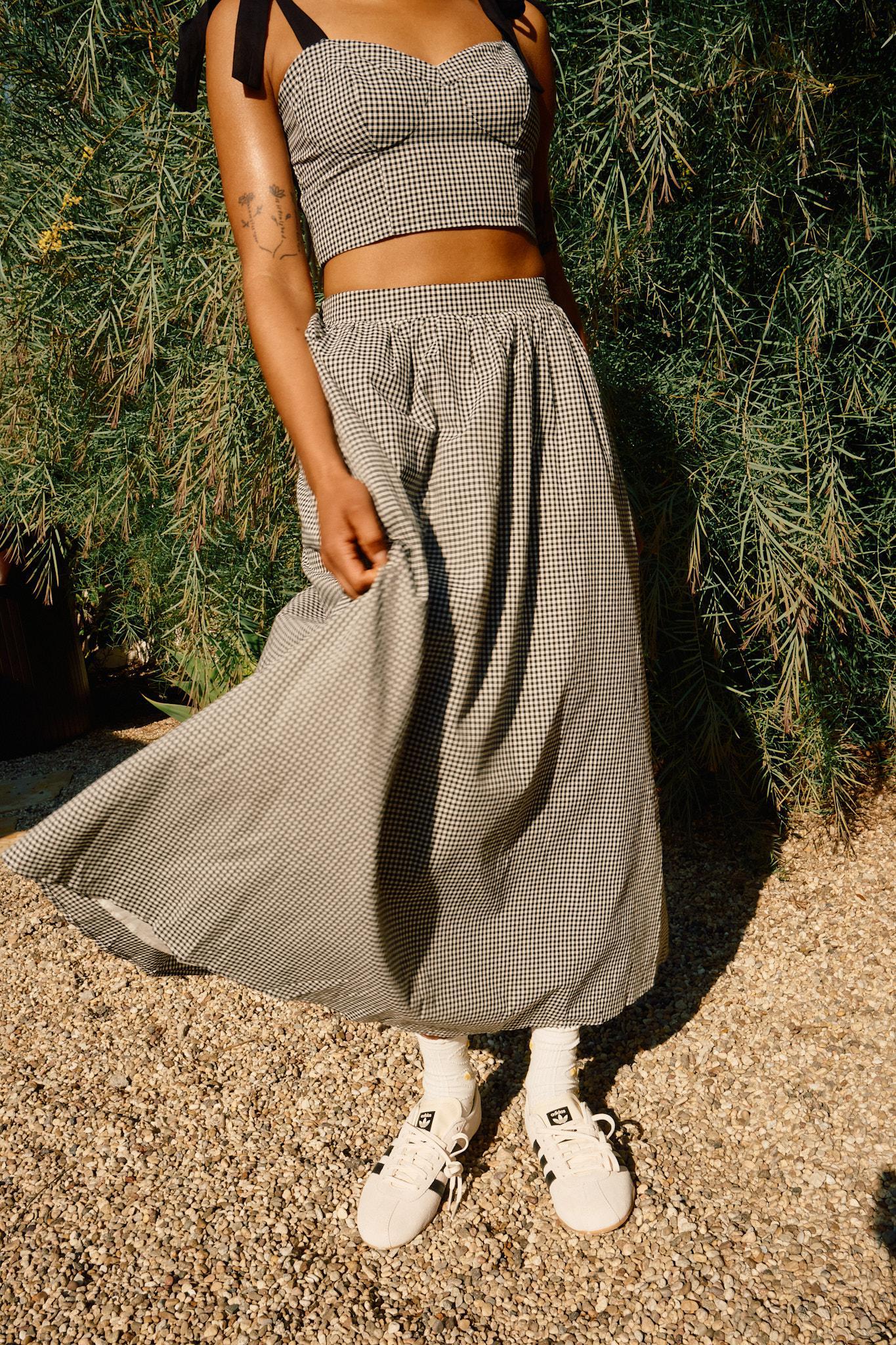 A person wearing a high rise black and white checkered maxi skirt with a crop top and white sneakers standing outdoors.