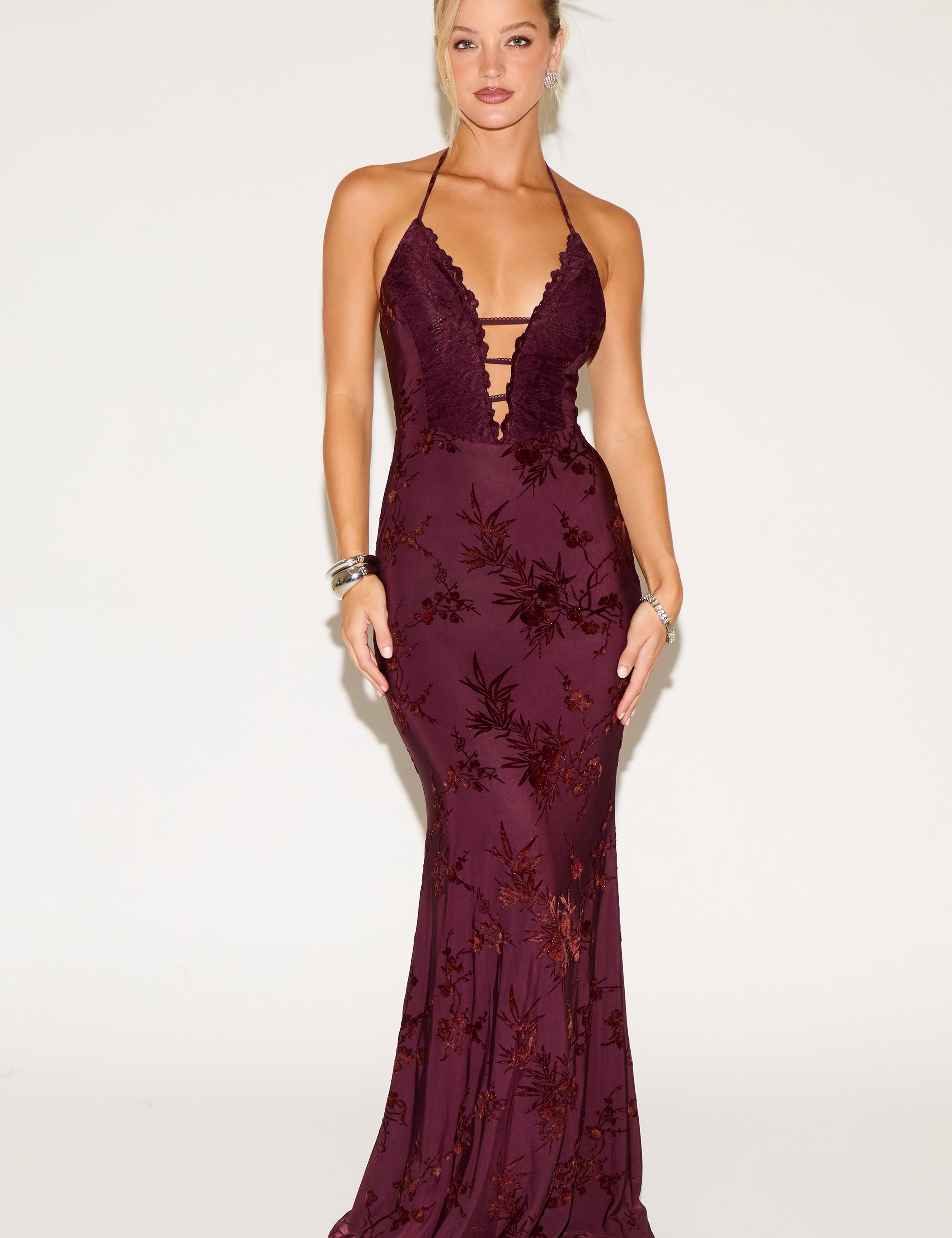 Woman wearing a burgundy evening gown with floral patterns on a white background