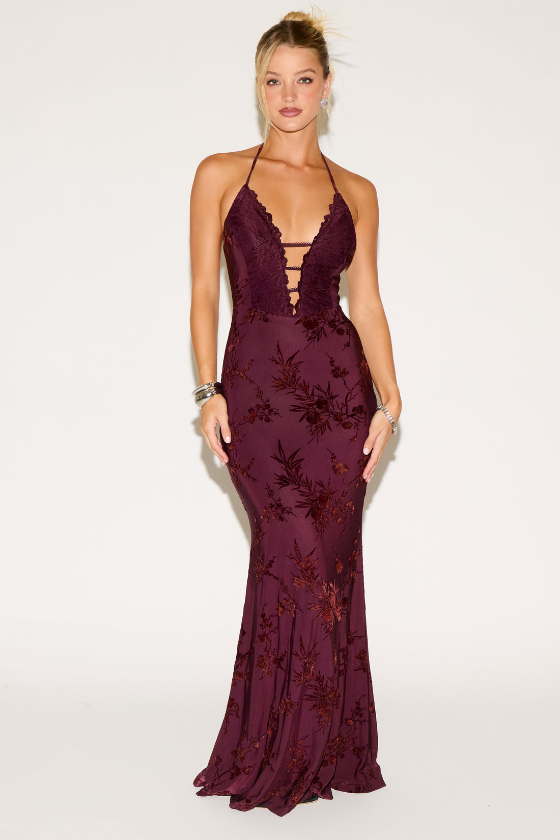 Woman wearing a deep purple evening gown with floral patterns on a white background