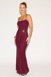 Woman wearing a burgundy evening gown with sequin details on a white background
