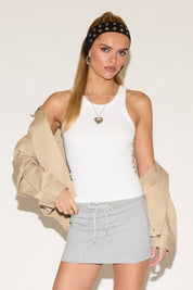 Model wearing a white tank top with a grey skirt and beige jacket. 