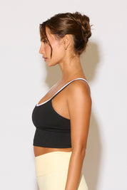 Woman wearing a black sports bra with white trim against a plain background