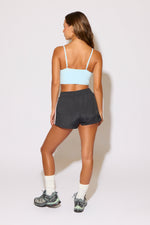 Woman wearing a light blue sports bra and dark gray shorts on a white background