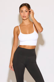 Woman wearing a white sports bra and black leggings against a light background