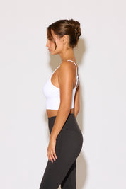 Woman wearing a white sports bra and black leggings against a light background