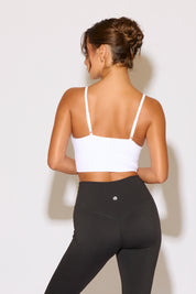 Woman wearing a white sports bra and black leggings against a light background