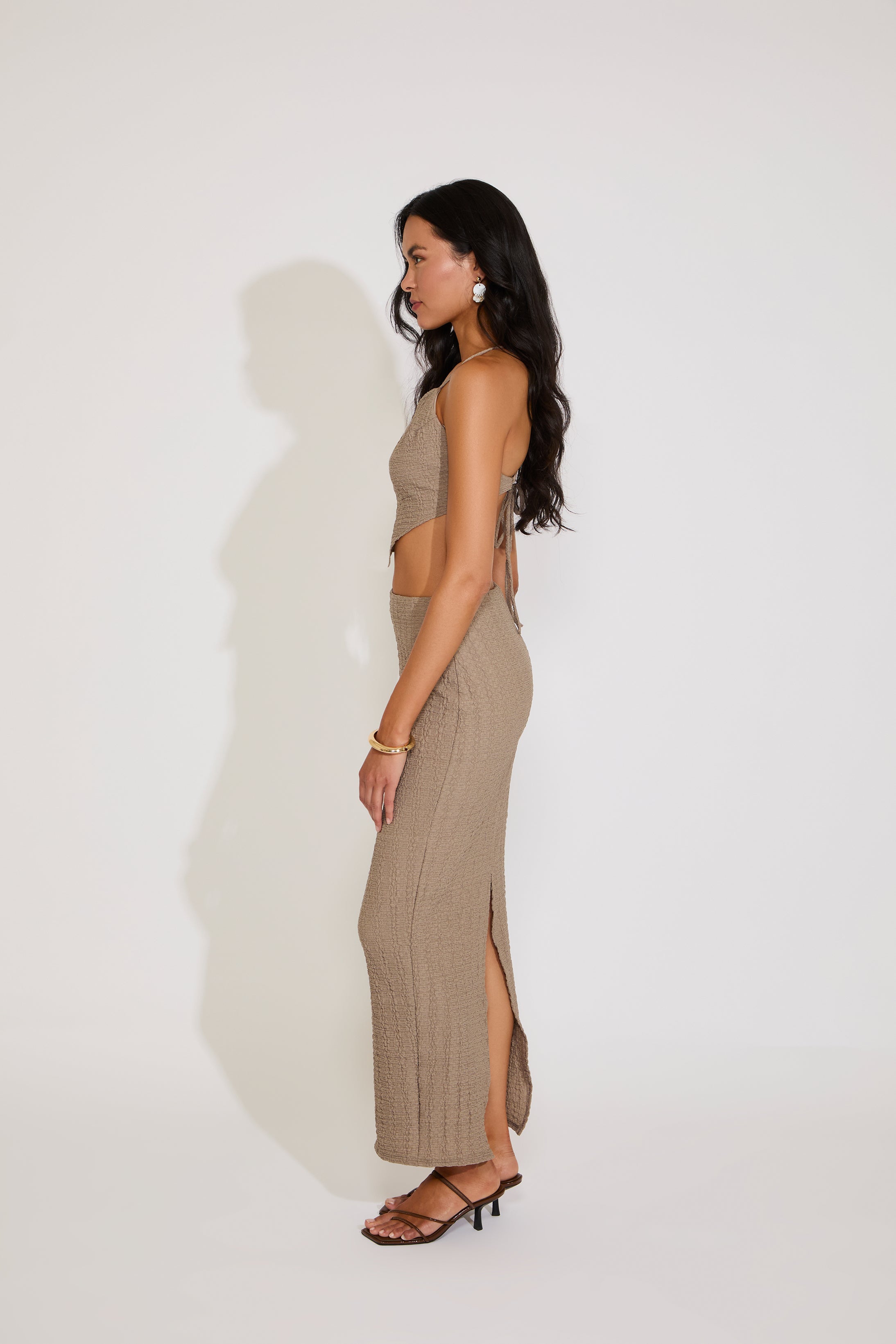 Woman wearing a beige halter top and long skirt on a white background