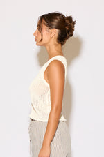 Woman wearing a white sleeveless top and gray pants against a white background