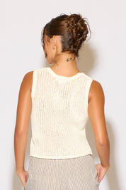 Woman wearing a white sleeveless top against a plain background