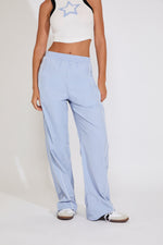 Person wearing light blue pants and a white crop top with a star design on a plain background