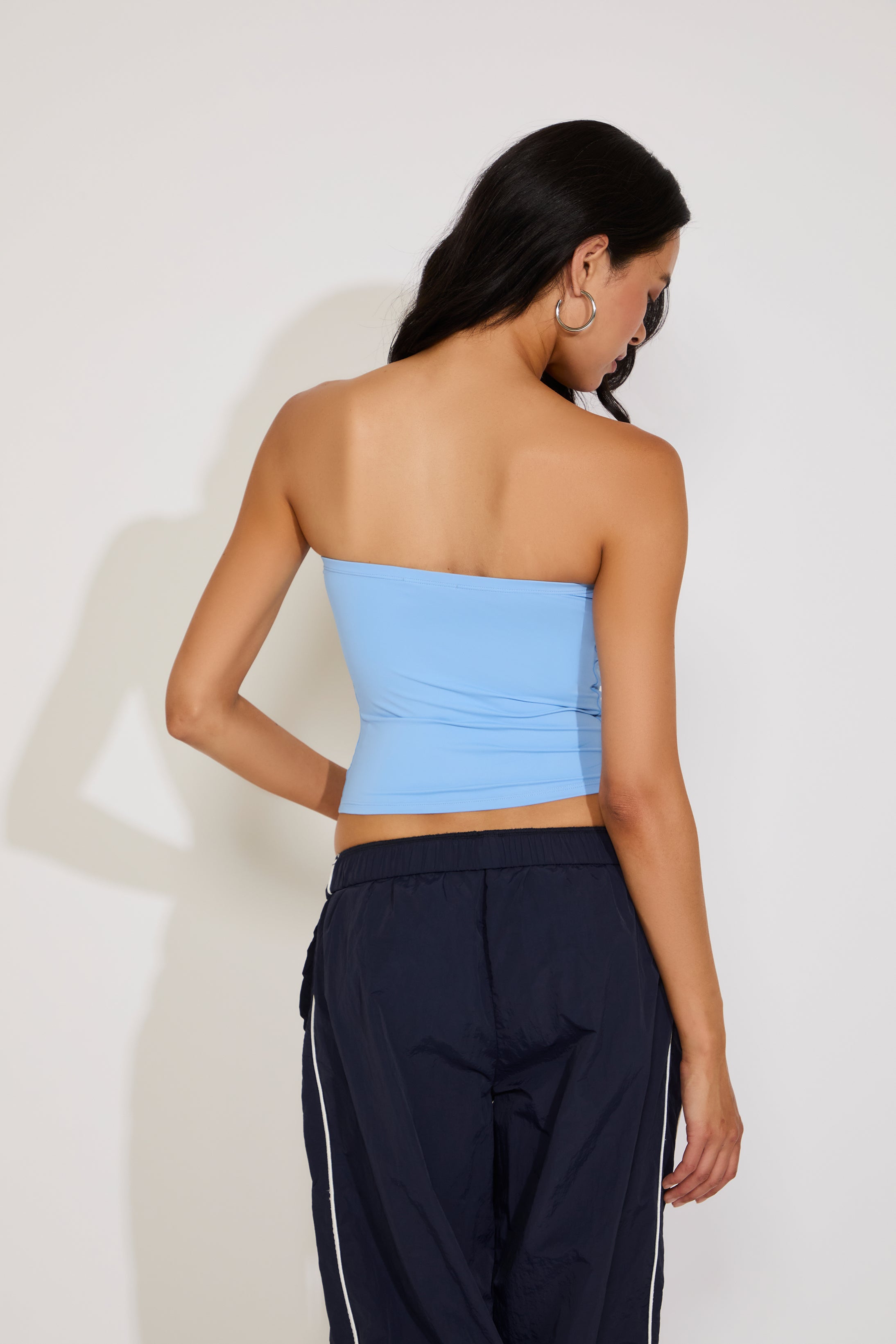 Woman wearing a light blue strapless top and dark pants against a white background