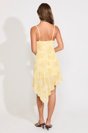 Model is wearing a yellow floral asymmetric drape mini dress on a white background.