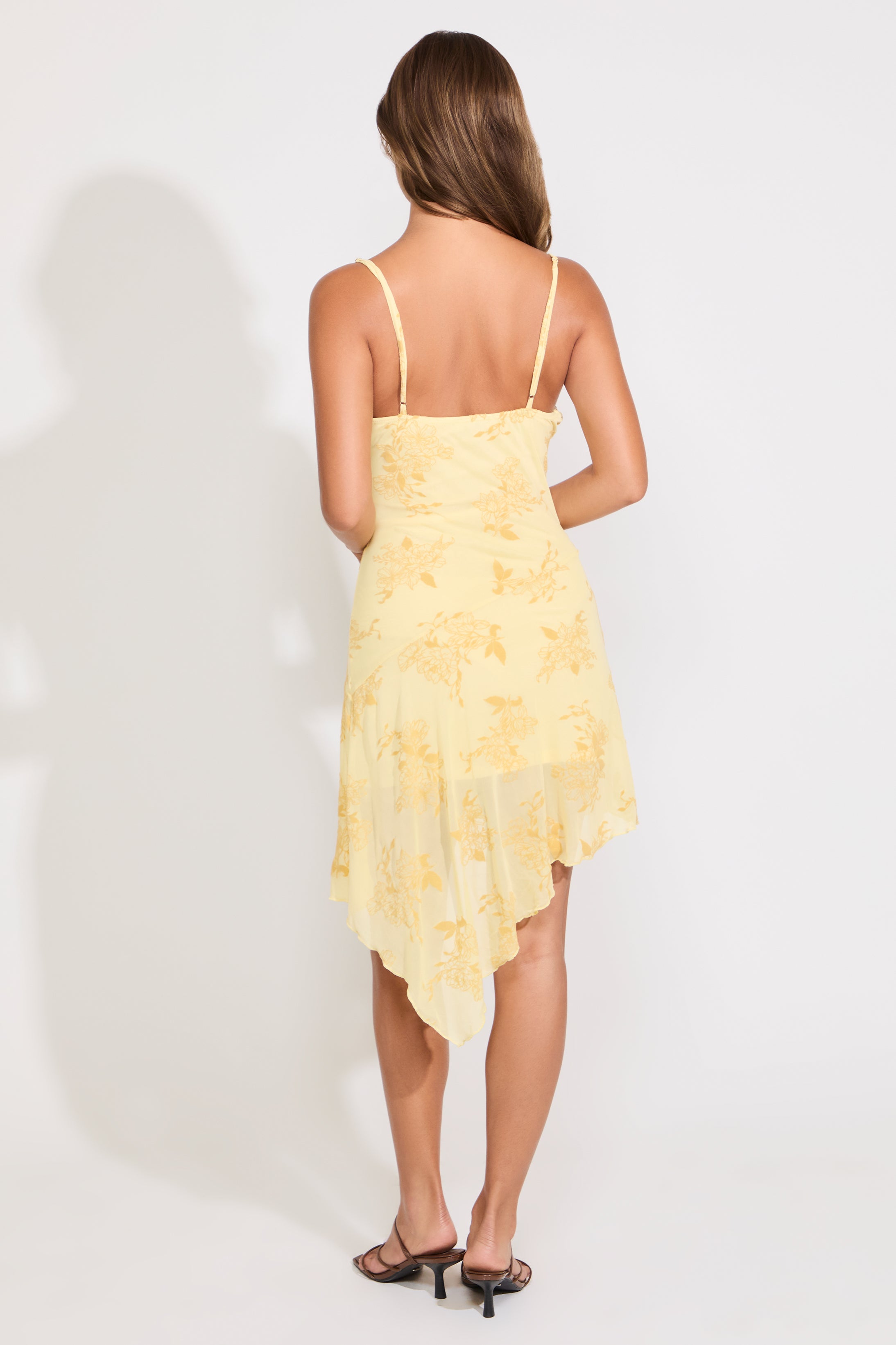 Model is wearing a yellow floral asymmetric drape mini dress on a white background.