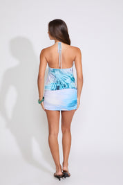 Model is wearing a lavender and blue INK BLOT HALTER KEYHOLE MINI DRESS WITH RUCHED SKIRT with black heels on a white background.