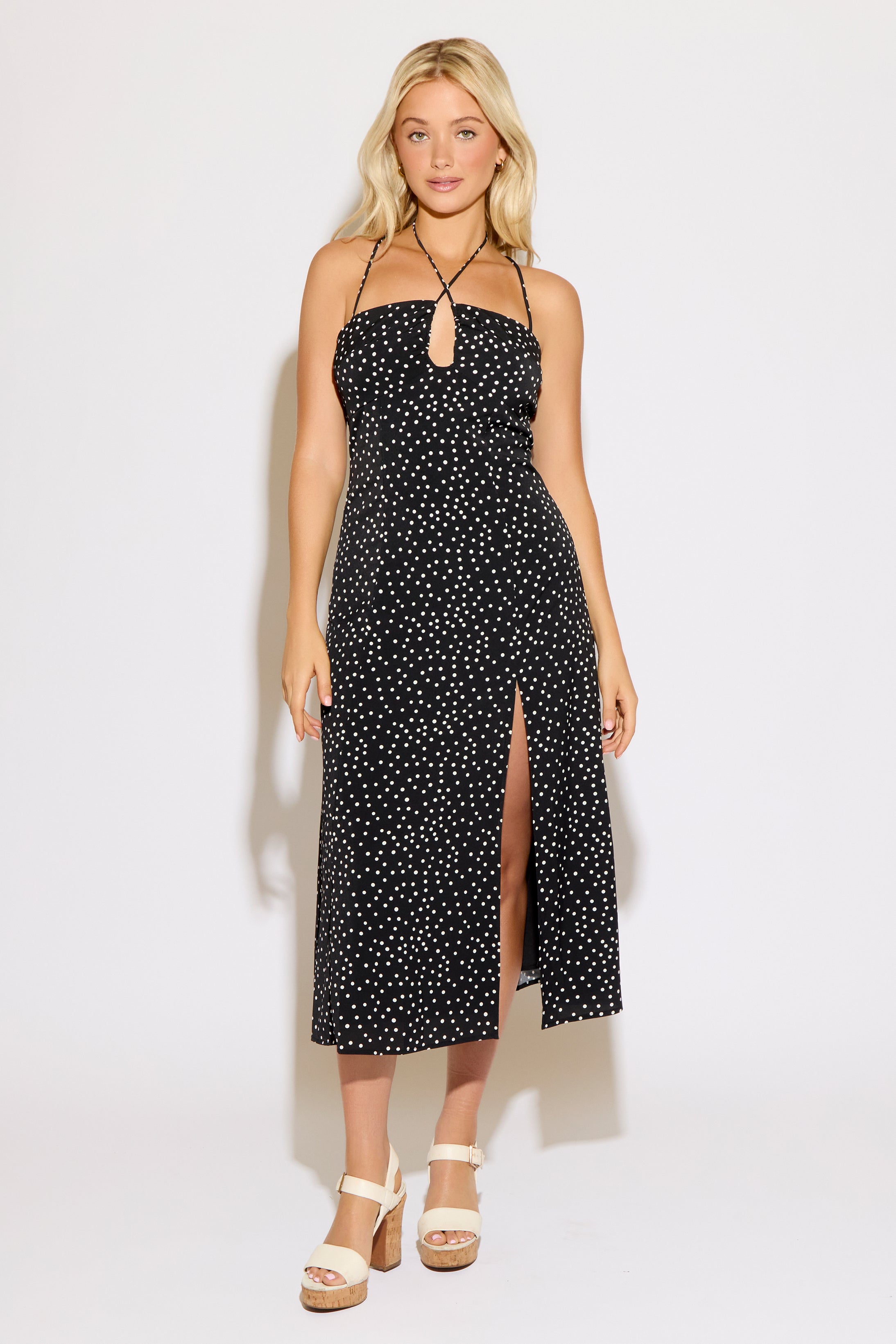 Model is wearing a black polka dot with a tie neck and cross back midi dress on a white background.