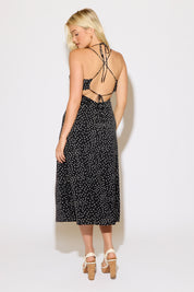 Model is wearing a black polka dot with a tie neck and cross back midi dress on a white background.