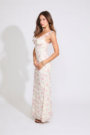 Model is wearing white and pink ROSE PRINT RUFFLE STRAP V NECK MAXI DRESS with black heels on a white background.