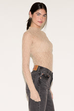 Woman wearing a beige turtleneck sweater and gray jeans on a plain background