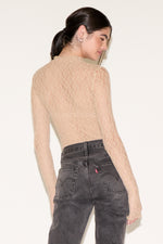 Person wearing a beige open-back sweater and gray jeans against a white background