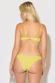 Model is wearing a textured mustard yellow with a gold ring detail bikini set on a white background.