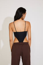 Woman wearing a black strappy top and brown pants against a white background