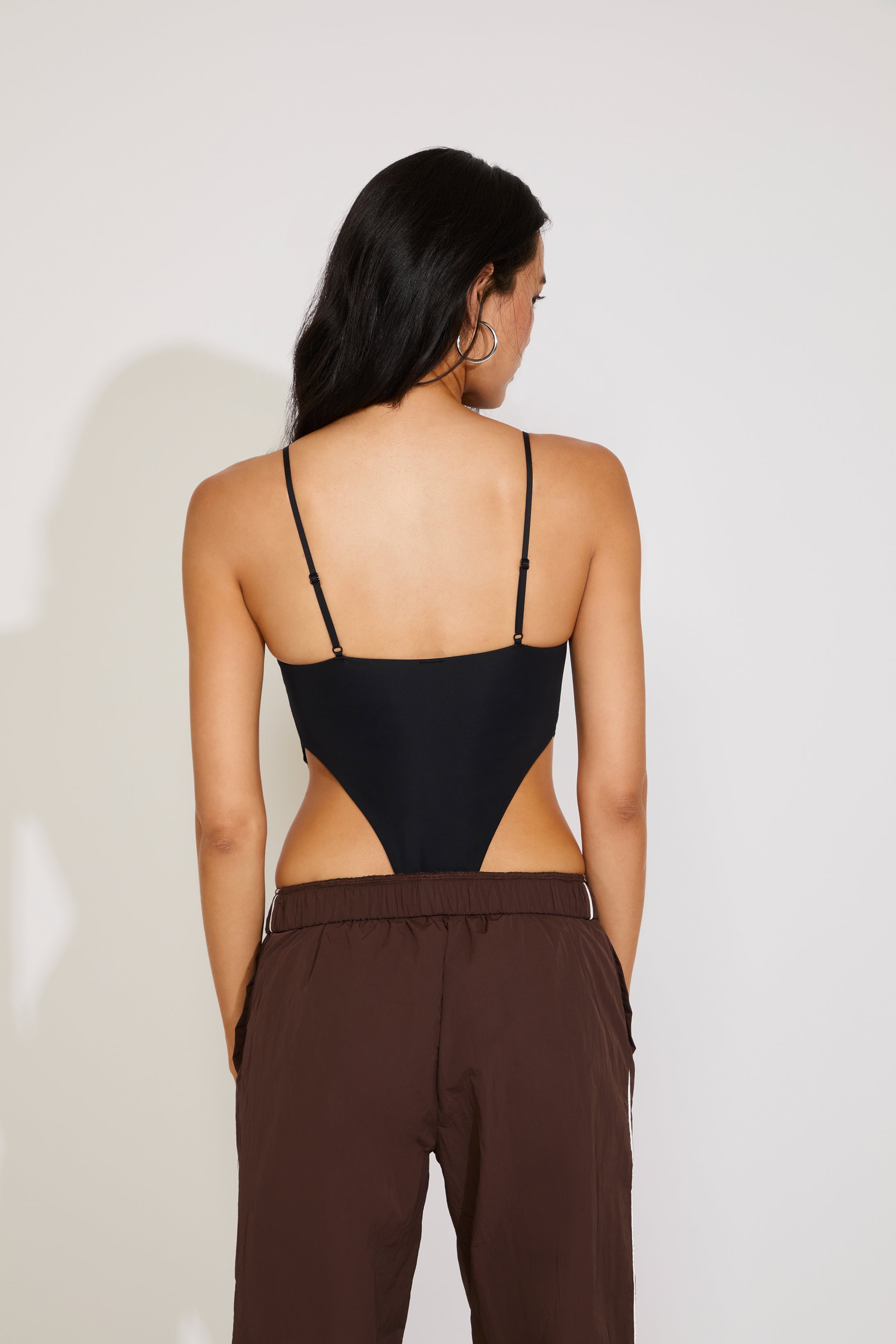 Woman wearing a black strappy top and brown pants against a white background