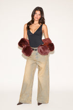 Woman wearing a black top, beige flared pants, and red fur gloves on a white background