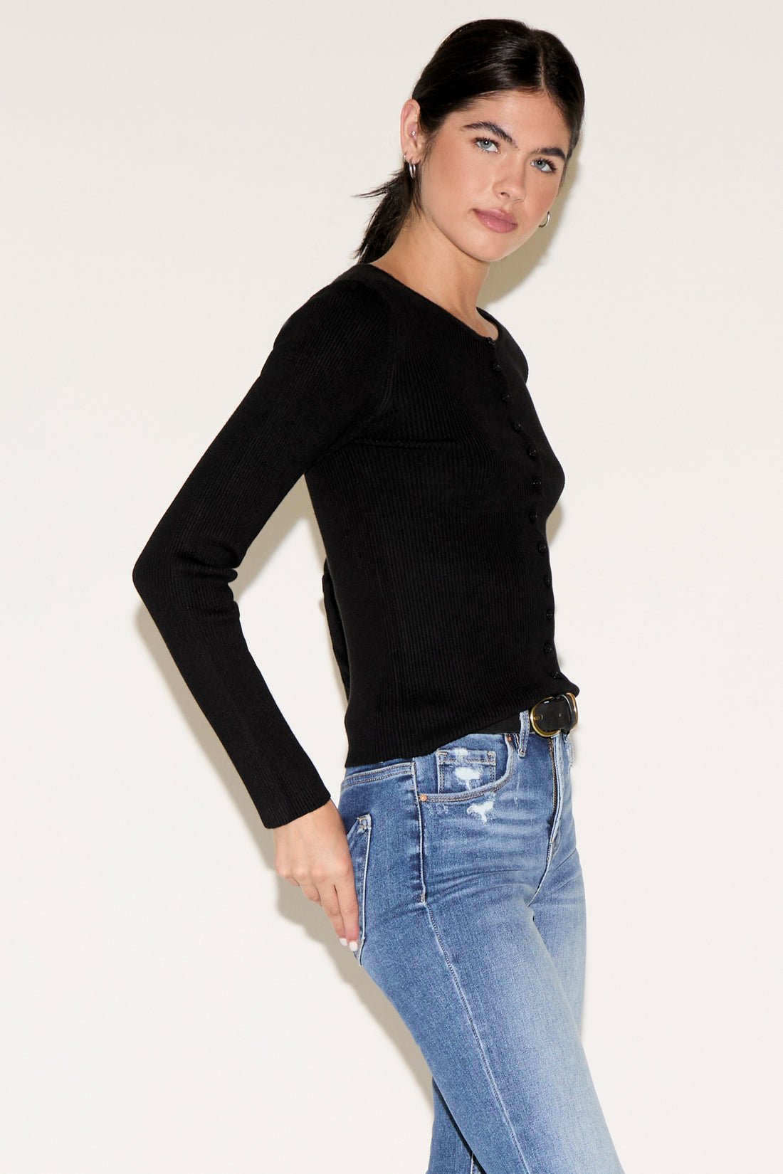 Woman wearing a black long-sleeve top and blue jeans against a white background