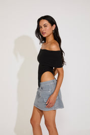 Woman wearing a black off-shoulder top and light blue denim skirt on a white background