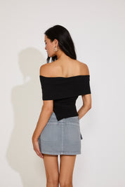 Woman wearing a black off-shoulder top and gray skirt against a white background