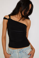 Woman wearing a black one-shoulder top and light blue jeans against a plain background