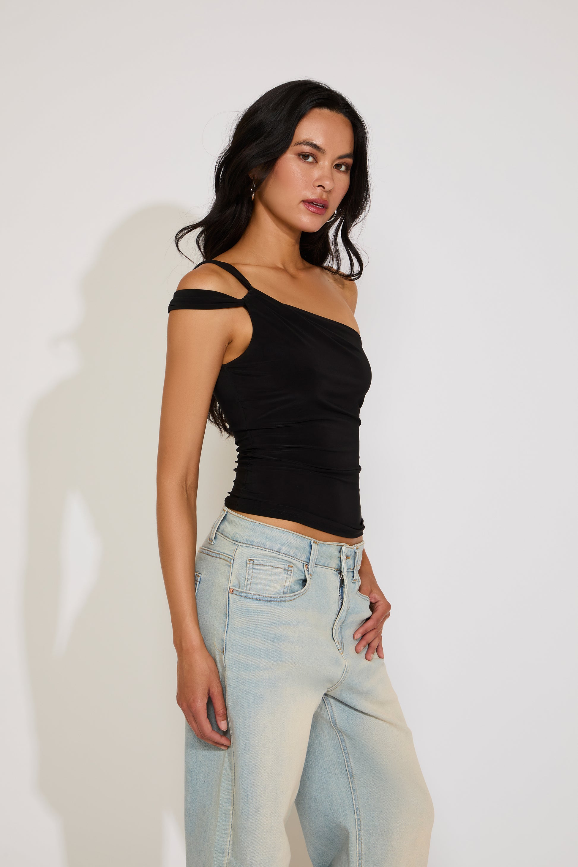Woman wearing a black top and light blue jeans against a white background
