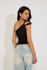 Woman wearing a black one-shoulder top and light blue jeans against a white background