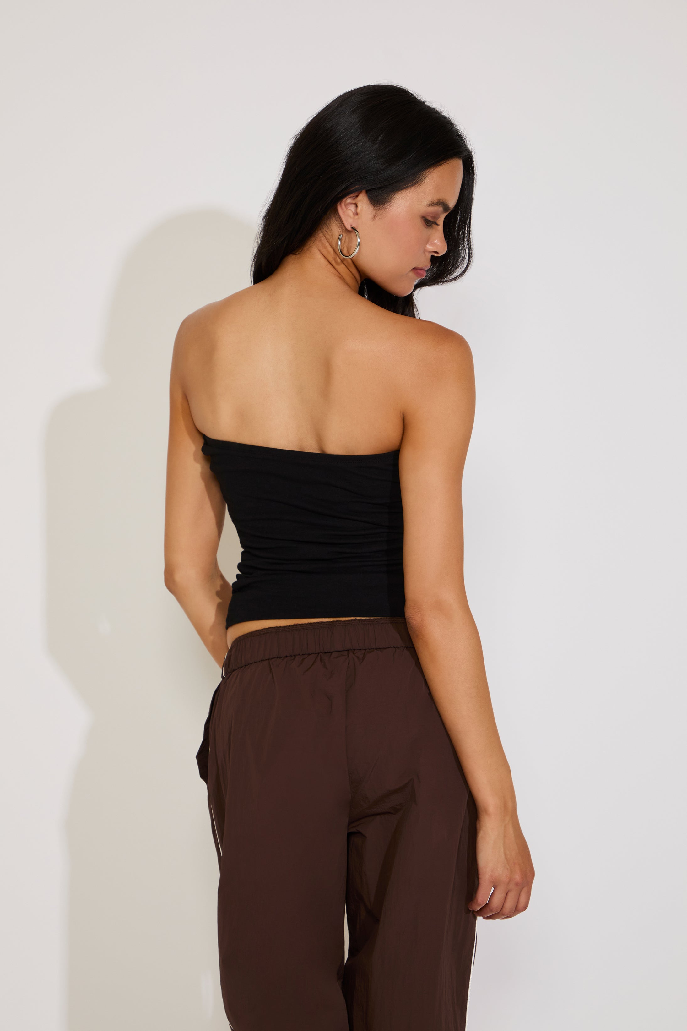 Woman wearing a black strapless top and brown pants against a white background