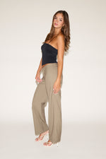 Woman wearing a black strapless top and beige wide-leg pants on a white background